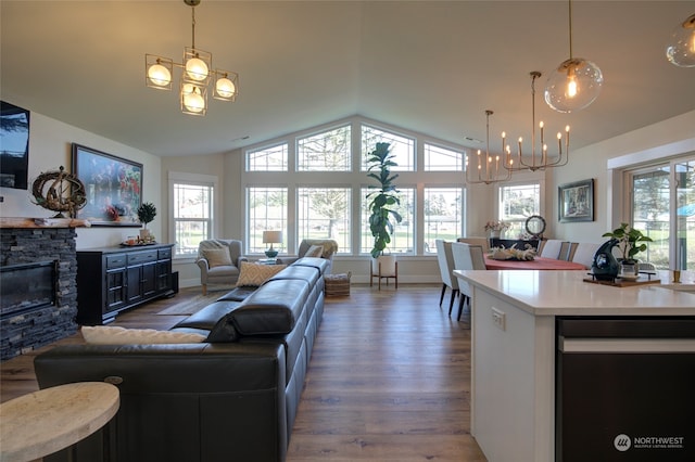 living room featuring an inviting chandelier, a stone fireplace, dark hardwood / wood-style flooring, and vaulted ceiling