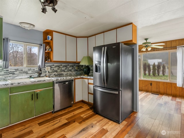 kitchen with light wood-type flooring, tasteful backsplash, stainless steel appliances, ceiling fan, and wooden walls