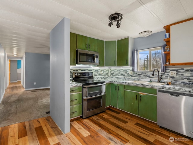 kitchen featuring sink, light hardwood / wood-style flooring, backsplash, appliances with stainless steel finishes, and green cabinetry