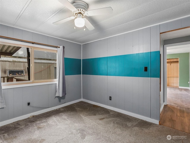 carpeted spare room featuring ceiling fan, wood walls, and a textured ceiling