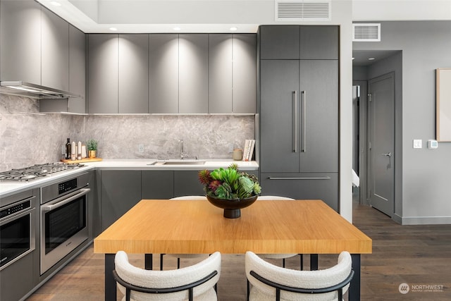 kitchen with backsplash, dark hardwood / wood-style flooring, stainless steel appliances, sink, and gray cabinets