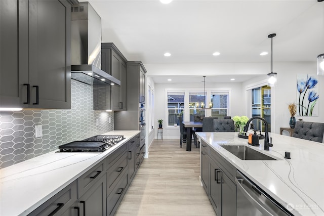 kitchen featuring appliances with stainless steel finishes, wall chimney exhaust hood, sink, decorative light fixtures, and light hardwood / wood-style floors