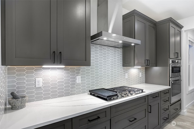 kitchen featuring light hardwood / wood-style flooring, wall chimney exhaust hood, gray cabinets, appliances with stainless steel finishes, and tasteful backsplash