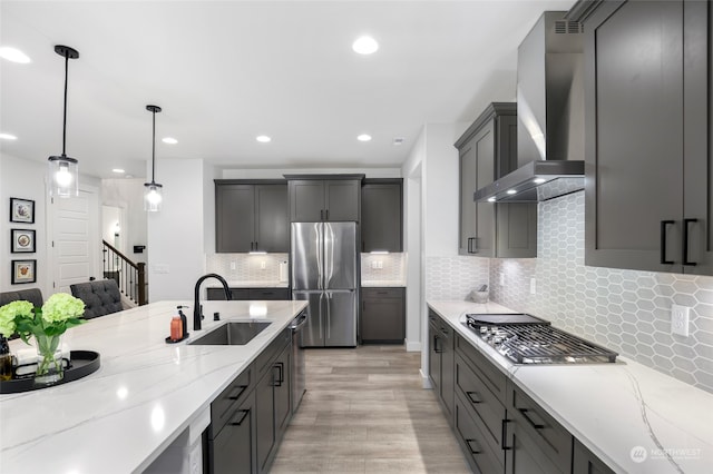 kitchen featuring wall chimney range hood, decorative light fixtures, decorative backsplash, appliances with stainless steel finishes, and light wood-type flooring