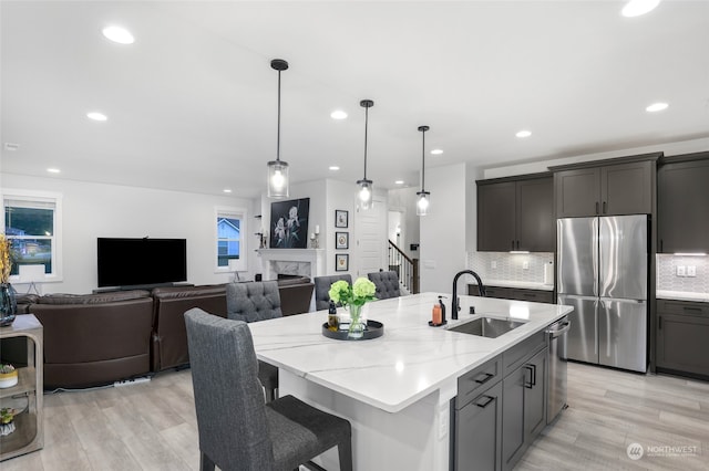 kitchen with a kitchen island with sink, sink, light stone countertops, light wood-type flooring, and appliances with stainless steel finishes