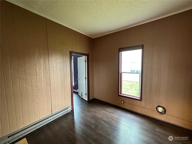 empty room with dark hardwood / wood-style floors, wood walls, a textured ceiling, and a baseboard heating unit