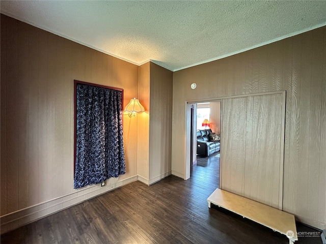 spare room featuring wooden walls, a textured ceiling, dark hardwood / wood-style floors, and ornamental molding