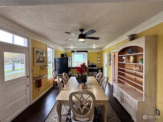 dining space with ceiling fan, wood walls, dark wood-type flooring, and a textured ceiling