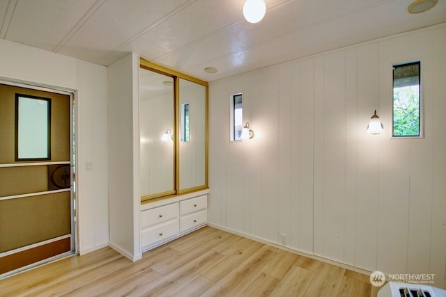 unfurnished bedroom with a closet, wooden walls, and light hardwood / wood-style flooring