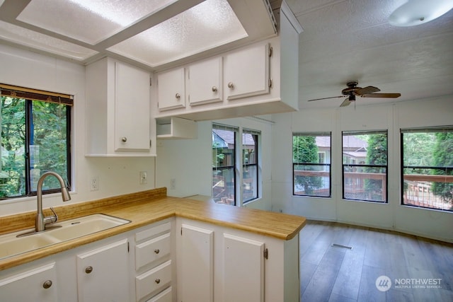 kitchen featuring kitchen peninsula, ceiling fan, sink, hardwood / wood-style flooring, and white cabinetry