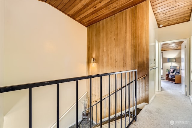 corridor with light carpet, wooden ceiling, and wood walls