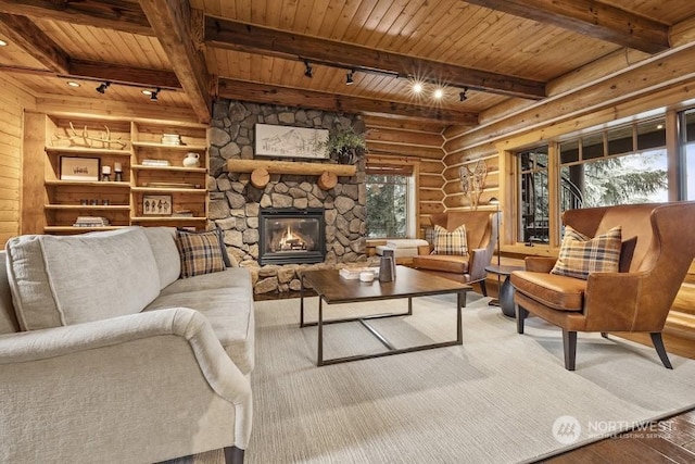 living room with a stone fireplace, log walls, rail lighting, and wooden ceiling