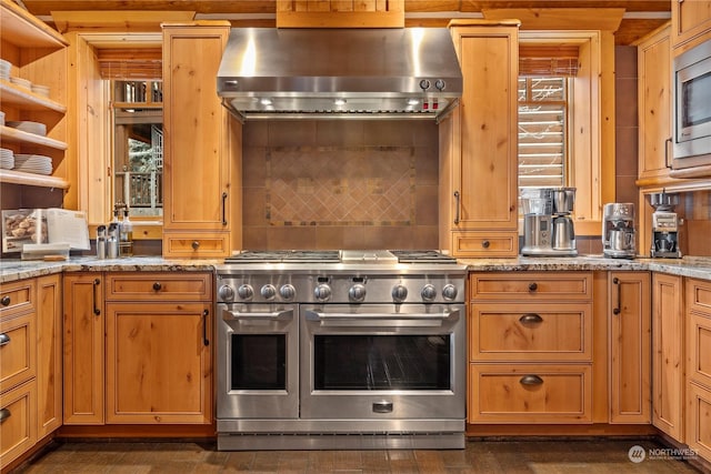 kitchen featuring light stone countertops, wall chimney range hood, and appliances with stainless steel finishes