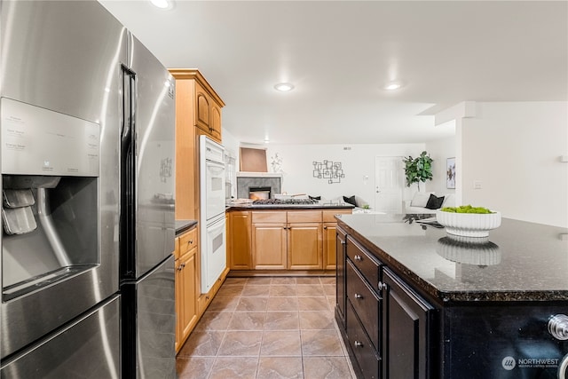 kitchen with white double oven, light brown cabinets, dark stone countertops, stainless steel fridge with ice dispenser, and a center island