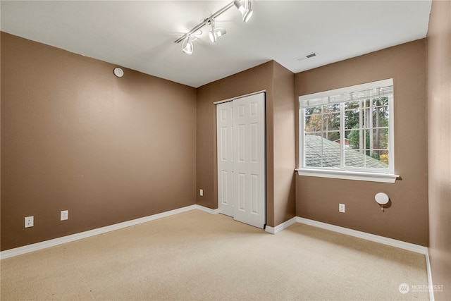 unfurnished bedroom with carpet flooring, track lighting, and a closet