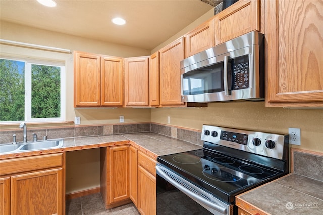 kitchen with appliances with stainless steel finishes, light tile patterned floors, tile counters, and sink