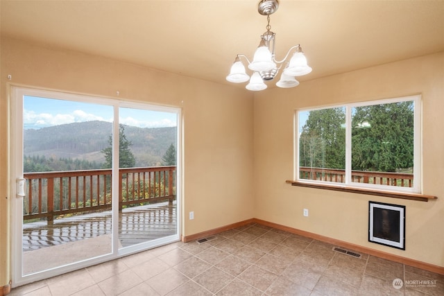 spare room with a mountain view, a wealth of natural light, a notable chandelier, and light tile patterned flooring