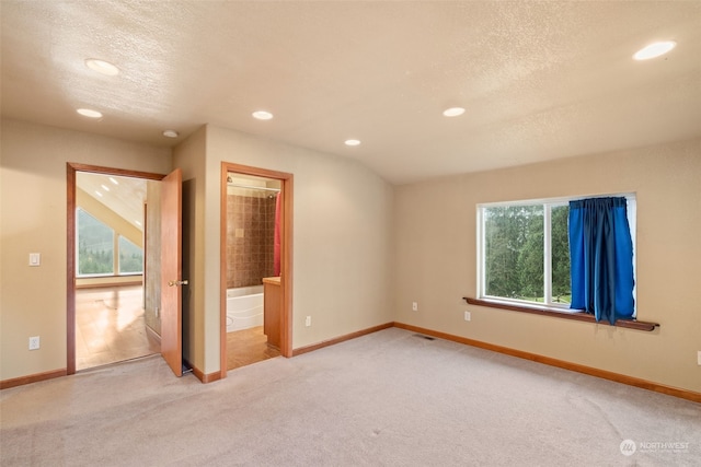 interior space with a textured ceiling, ensuite bathroom, and light carpet