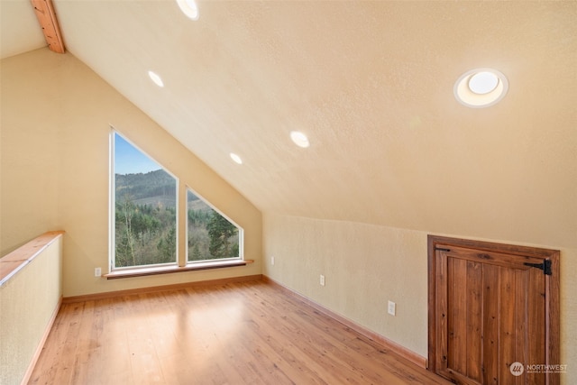 additional living space with light wood-type flooring and lofted ceiling with beams