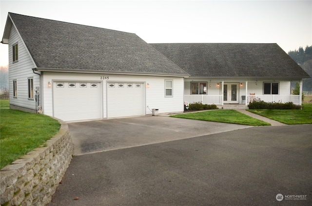 view of front of house featuring french doors, a porch, a garage, and a front lawn