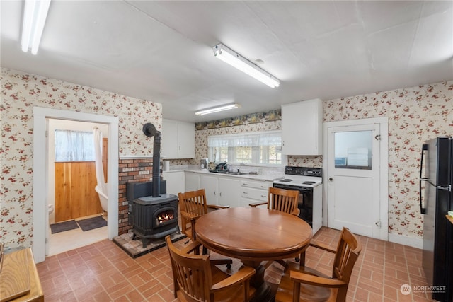 kitchen featuring sink, electric stove, white cabinetry, a wood stove, and stainless steel refrigerator