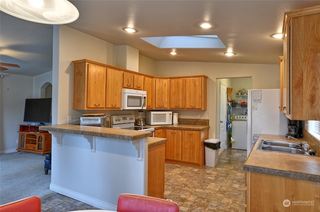 kitchen with white appliances, a kitchen breakfast bar, sink, washer / dryer, and kitchen peninsula