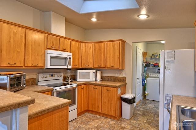 kitchen featuring vaulted ceiling with skylight, white appliances, sink, and washer / clothes dryer