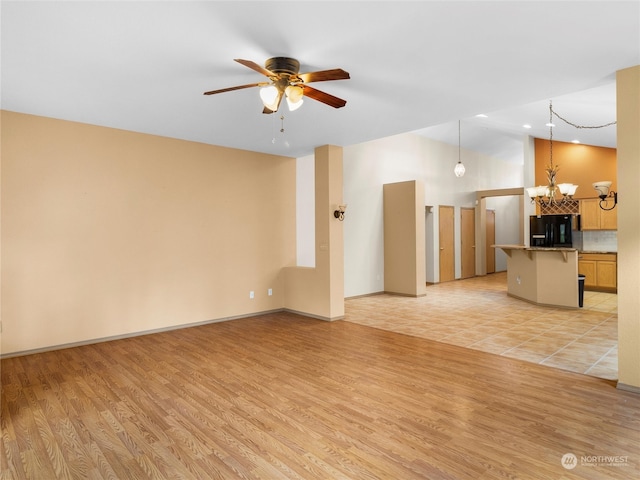 unfurnished living room with ceiling fan with notable chandelier and light hardwood / wood-style flooring