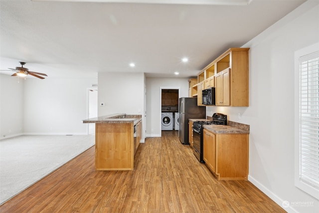 kitchen featuring black appliances, washer and clothes dryer, light hardwood / wood-style floors, and ceiling fan