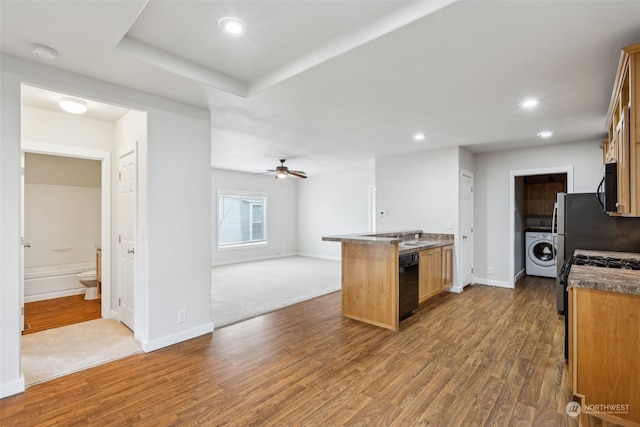 kitchen featuring hardwood / wood-style floors, black appliances, sink, ceiling fan, and washer / dryer