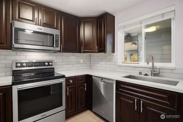 kitchen featuring backsplash, sink, light tile patterned floors, dark brown cabinets, and stainless steel appliances