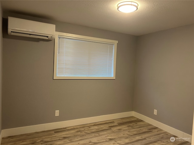 unfurnished bedroom featuring an AC wall unit, a textured ceiling, and light hardwood / wood-style flooring