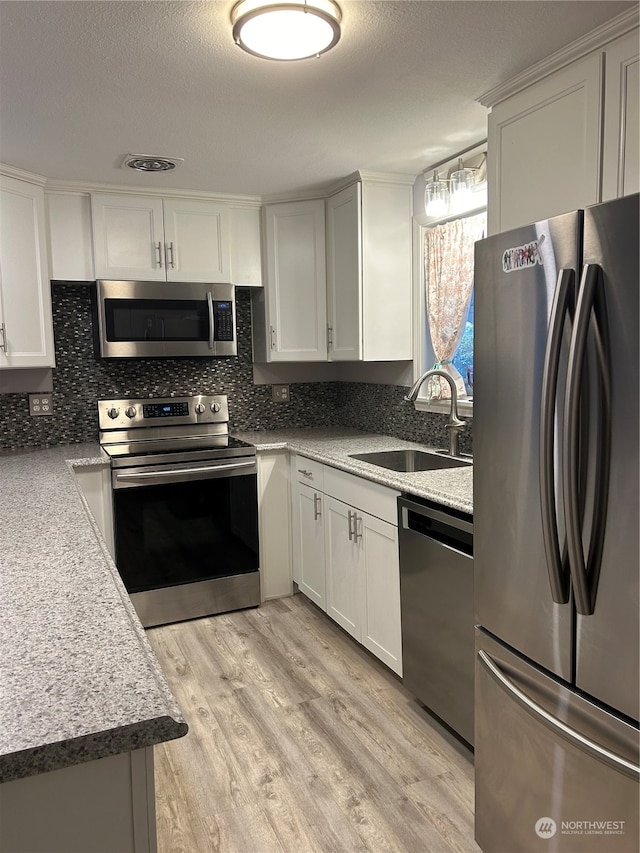 kitchen with white cabinetry, sink, stainless steel appliances, decorative backsplash, and light wood-type flooring