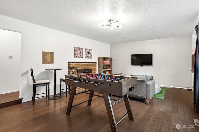 rec room with a fireplace, a textured ceiling, dark hardwood / wood-style floors, and a notable chandelier