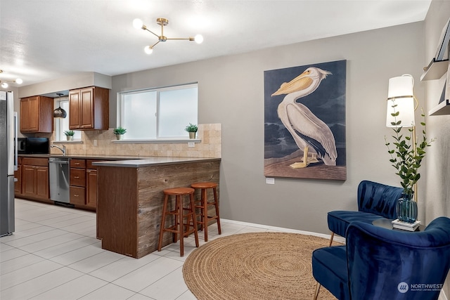 kitchen with kitchen peninsula, appliances with stainless steel finishes, tasteful backsplash, light tile patterned floors, and a breakfast bar area