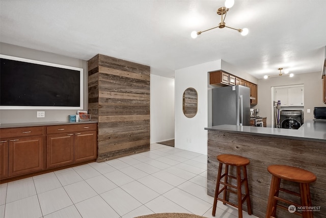 kitchen featuring a kitchen bar, stainless steel fridge, wooden walls, washer / dryer, and light tile patterned flooring