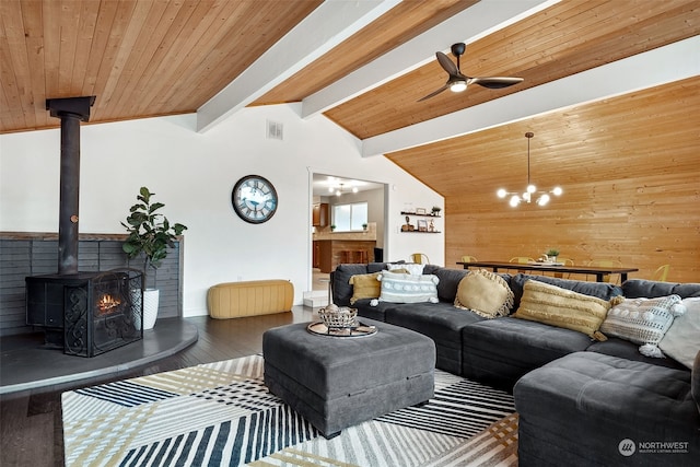 living room featuring hardwood / wood-style floors, a wood stove, ceiling fan with notable chandelier, wooden walls, and vaulted ceiling with beams