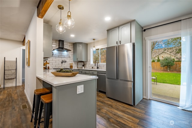 kitchen featuring wall chimney exhaust hood, dark hardwood / wood-style floors, a breakfast bar, and appliances with stainless steel finishes