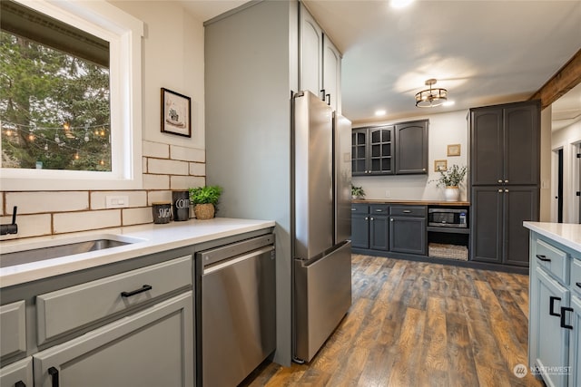 kitchen featuring gray cabinetry, dark wood-type flooring, sink, decorative backsplash, and appliances with stainless steel finishes