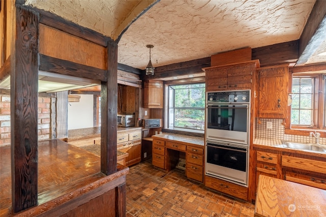 kitchen with a textured ceiling, stainless steel double oven, tasteful backsplash, and sink