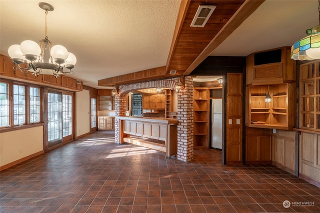 kitchen with ornate columns, an inviting chandelier, wood walls, refrigerator, and a textured ceiling