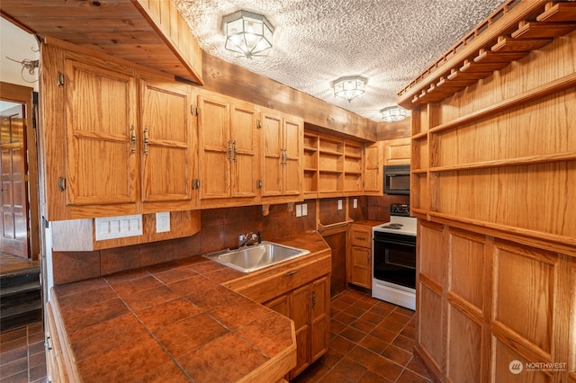 kitchen featuring sink, tile counters, white range with electric stovetop, a textured ceiling, and wooden walls