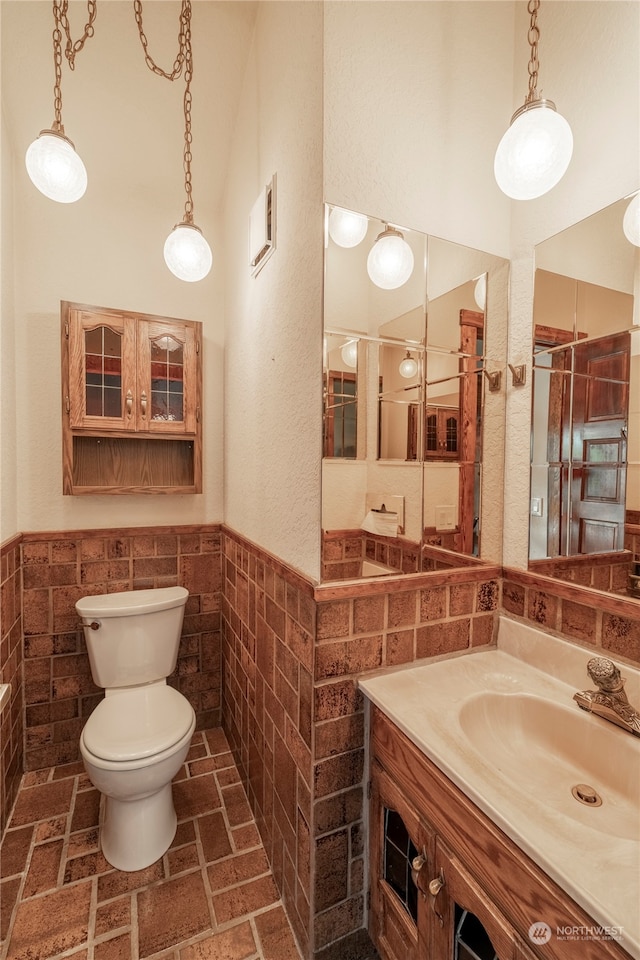 bathroom featuring a high ceiling, vanity, toilet, and tile walls