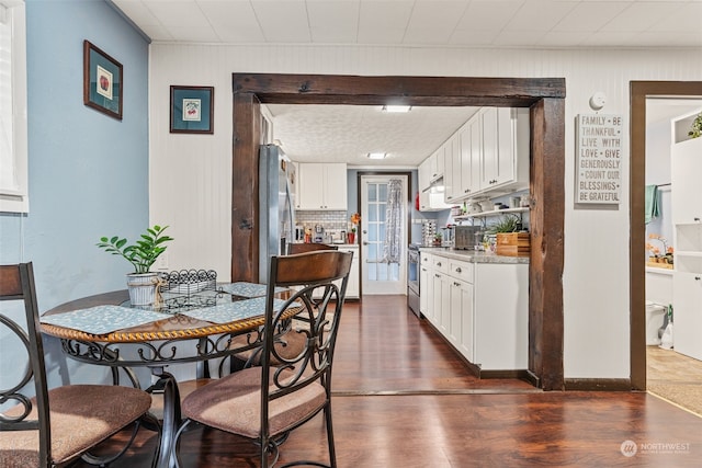 kitchen with white cabinetry, dark wood-type flooring, light stone counters, backsplash, and appliances with stainless steel finishes