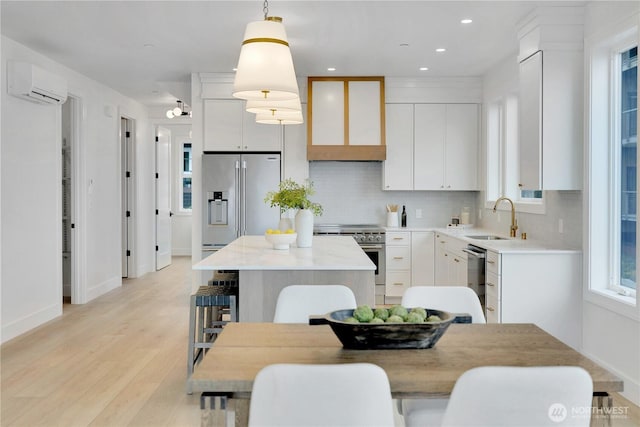 kitchen with a sink, high end appliances, light wood-type flooring, a kitchen island, and a wall mounted AC