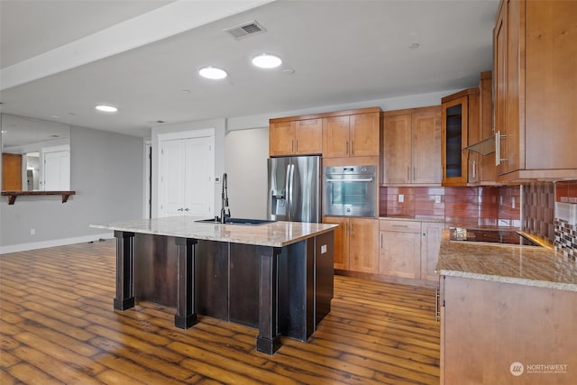 kitchen with appliances with stainless steel finishes, backsplash, a kitchen island with sink, sink, and wood-type flooring