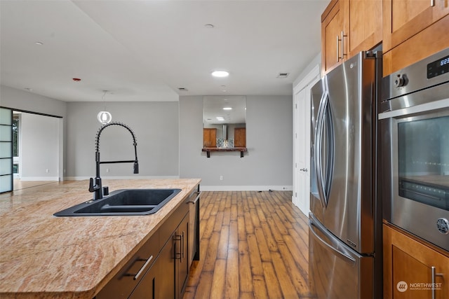 kitchen featuring sink, light hardwood / wood-style flooring, an island with sink, appliances with stainless steel finishes, and light stone counters