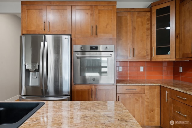 kitchen featuring decorative backsplash, sink, light stone countertops, and stainless steel appliances