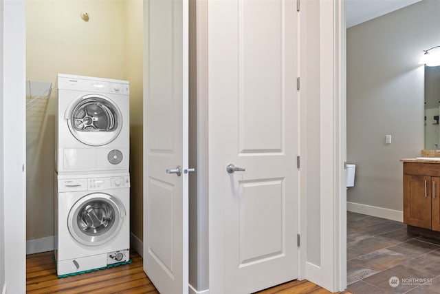 laundry room featuring dark hardwood / wood-style floors, stacked washer / dryer, and sink