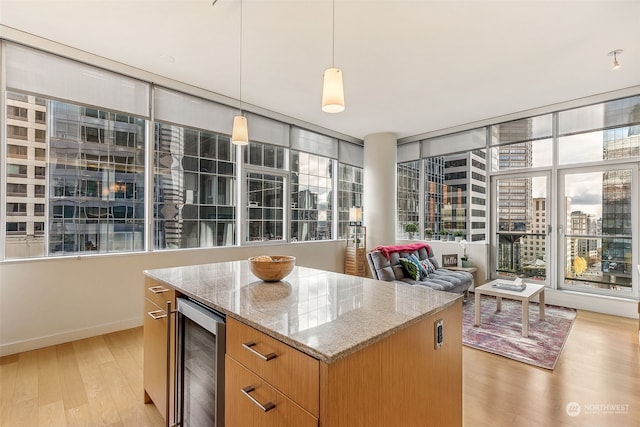 kitchen with hanging light fixtures, light hardwood / wood-style flooring, a kitchen island, light stone counters, and beverage cooler